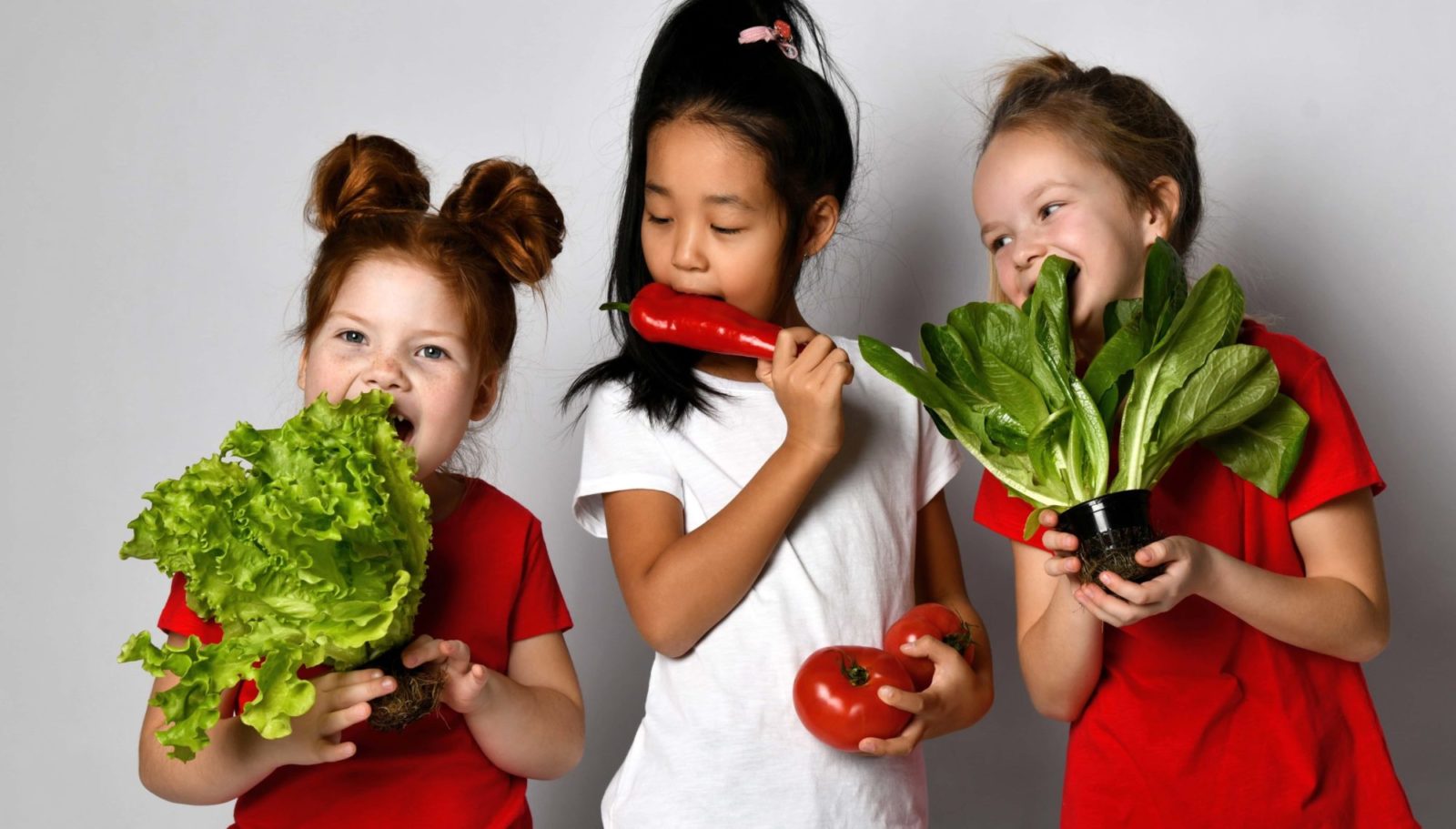 three happy girls are holding vegatables